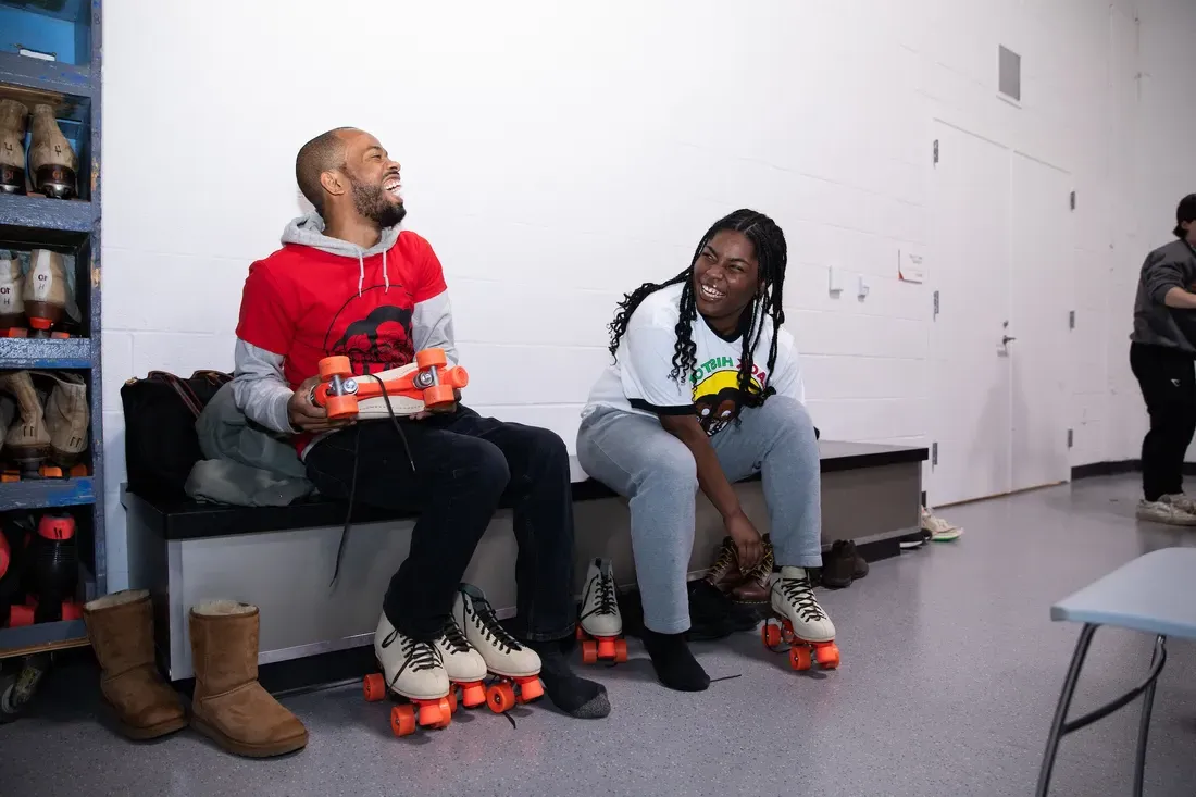 People sitting on a bench and laughing with roller skates on.